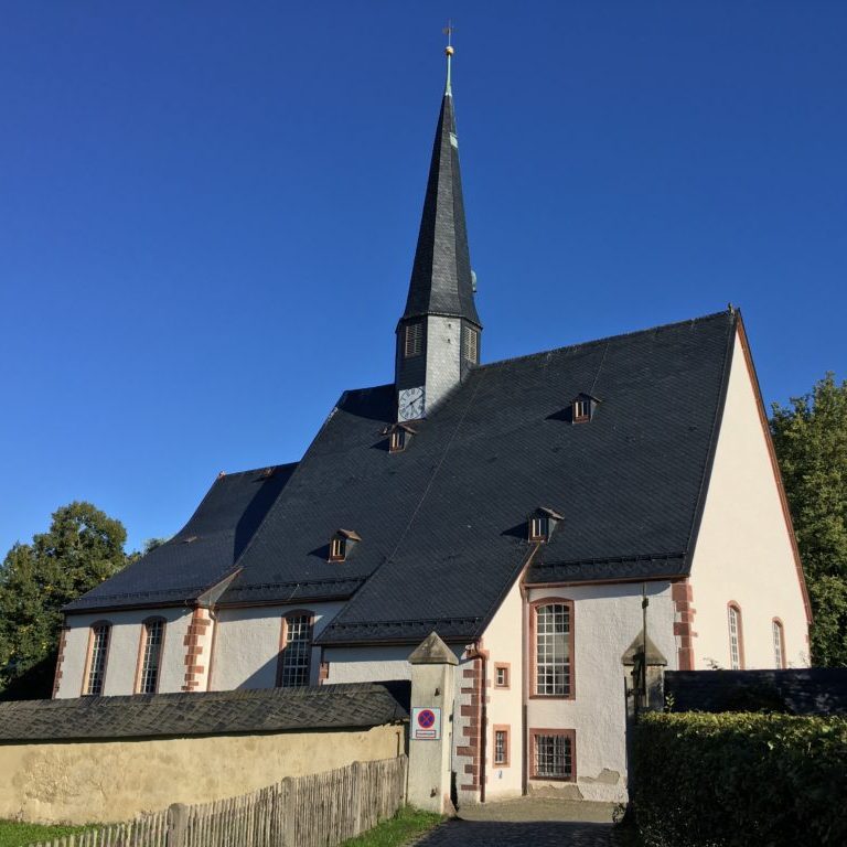 Feldsteinkirche mit spitzem Turm vor blauem Himmel und grüner Umgebung.