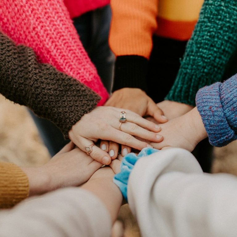 Verschränkte Hände in bunten Pullovern, die Gemeinschaft und Zusammenhalt zeigen.